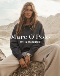 Gisele Bundchen wearing a dark grey hoodie and light trousers outdoors against a sandy terrain background.