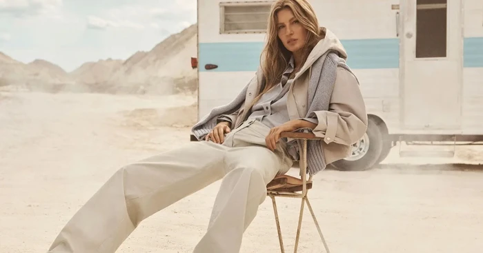 Gisele Bündchen seated on a folding chair in front of a trailer in a desert landscape for Marc O'Polo Spring 2026 campaign.