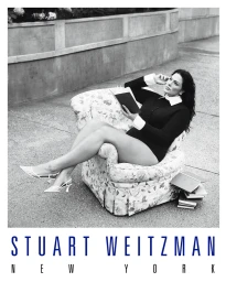 Ashley Graham seated in an armchair outdoors holding a book for the Stuart Weitzman Concrete Paradise campaign.