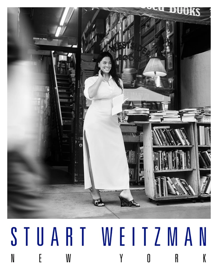 Ashley Graham standing outside a bookstore in a white dress and wedges for Stuart Weitzman