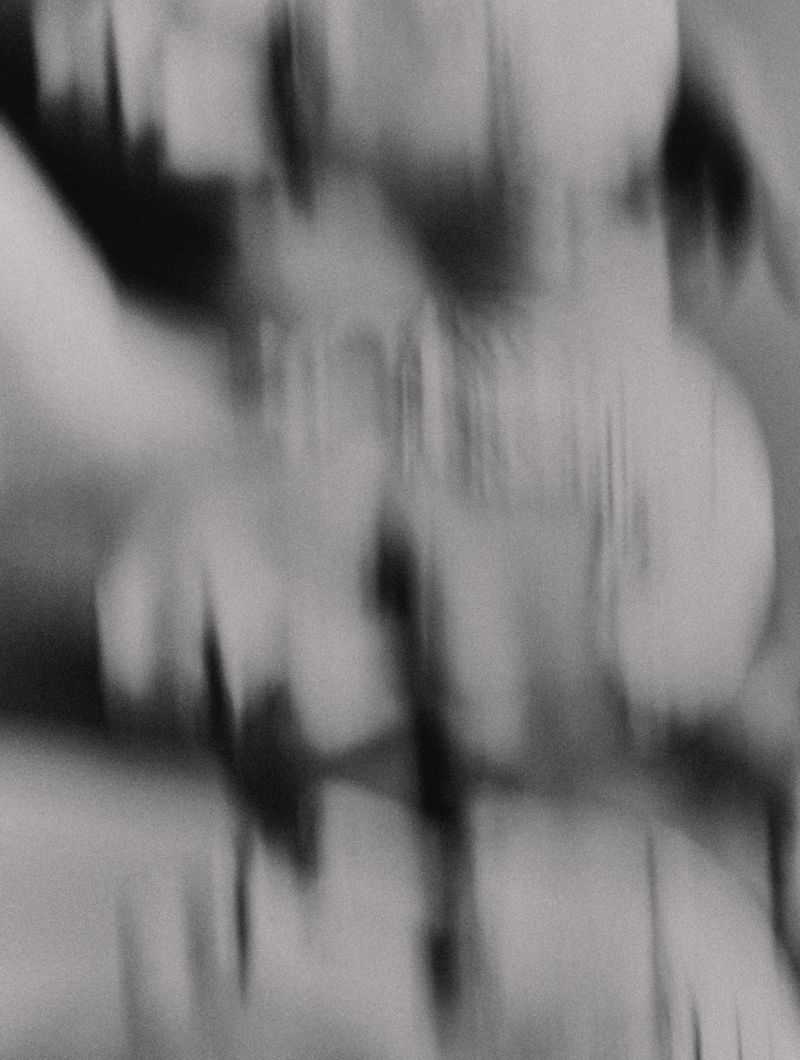 Abstract monochrome long exposure of blurred figures, creating a dynamic and mysterious visual effect, possibly from a dance performance.