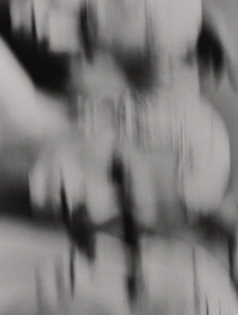 Abstract monochrome long exposure of blurred figures, creating a dynamic and mysterious visual effect, possibly from a dance performance.