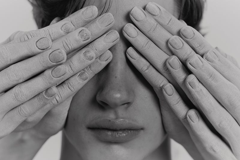 Close-up black and white portrait of face with hands covering eyes, featuring skin details, nail texture, and monochrome tonality.