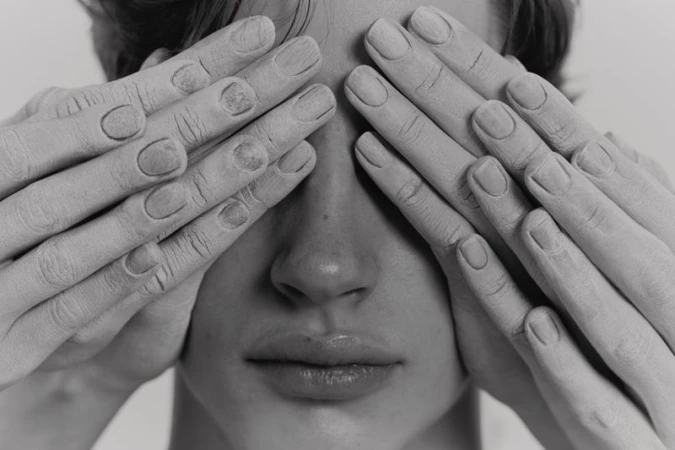 Close-up black and white portrait of face with hands covering eyes, featuring skin details, nail texture, and monochrome tonality.