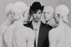 Group of shirtless men with white-painted hair surrounding a central man in a dark jacket and hat for The Rakish Gent