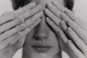 Black and white close-up portrait of a young man with hands coated in chalky powder placed over his eyes.