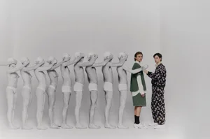 Two living models standing beside a line of painted white human statues in a studio setting