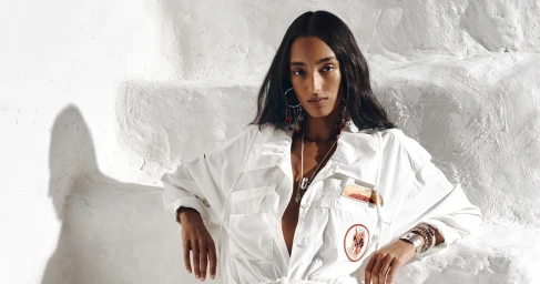 Model Mona Tougaard wearing white utility shirt and layered jewelry posing against textured white background.
