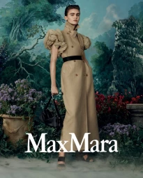 Model wearing a tan belted trench coat with ruffled short sleeves standing before a painted landscape backdrop