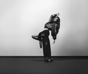 Jennie in a dynamic pose wearing a dark athletic jacket and trousers against a neutral background for Adidas Hotel Superstar