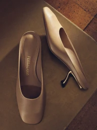 A pair of neutral beige leather mules with slender heels resting on a muted surface in a product shot for Salvatore Ferragamo.