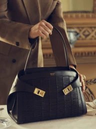 Model holding a structured black leather handbag with gold hardware for Salvatore Ferragamo