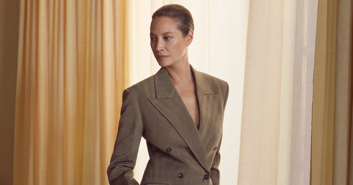 Christy Turlington wearing a tailored taupe blazer standing indoors against draped curtains for Salvatore Ferragamo
