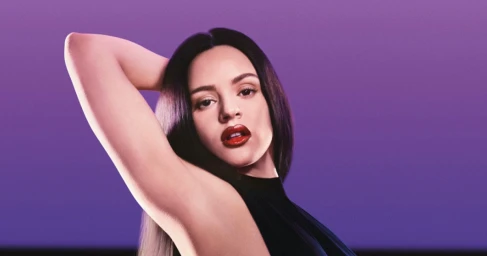 Rosalia posing with arm raised in a commercial portrait for Calvin Klein against a solid purple background