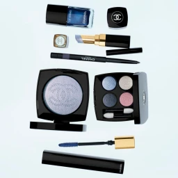 Flat lay of Chanel makeup products including nail polish, eyeshadow palettes, and lipstick on a light blue background.