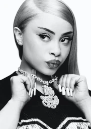 Portrait of Ice Spice wearing a large diamond pendant necklace and dark top against a plain white background.