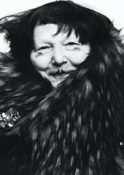 Close-up monochrome portrait of Lynn Yaeger wearing a dark faux fur collar against a white background