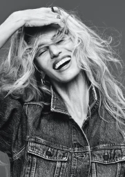 Black and white portrait of a smiling woman with long flowing hair wearing a denim jacket, photographed by Rafael Pavarotti for H&M.