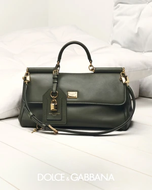Dark green leather handbag with gold hardware resting on white pillows against a clean white background