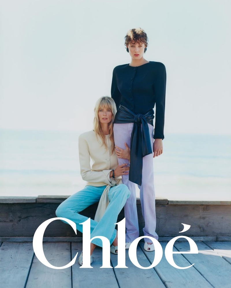 Two models posing on a wooden pier by the sea in tailored pastels and black knitwear for Chloé.