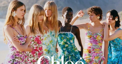 Six models in floral print summer dresses posing outdoors against a sandy beach background for Chloé