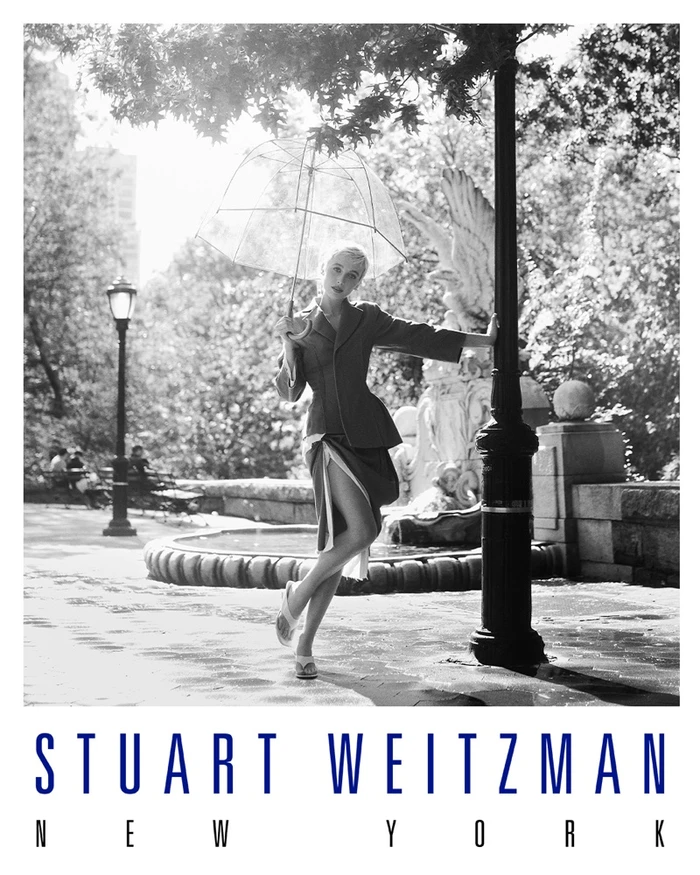Emma Chamberlain holding a transparent umbrella in a park leaning against a lamp post for Stuart Weitzman