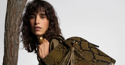 Model Mica Arganaraz holding a snakeskin handbag against a plain background for the Michael Kors Spring 2026 campaign.