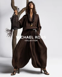 Model Mica Arganaraz in a brown outfit posing by a tree branch for Michael Kors Spring 2026 campaign.