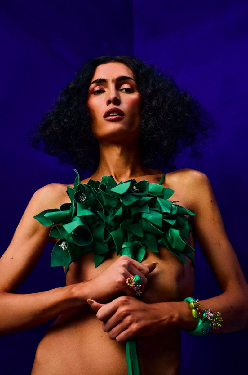 Model Mina Serrano holding a green floral sculpture against a deep blue background for Elle Mexico Protect The Dolls project.