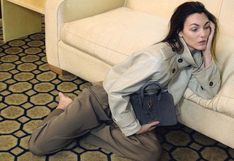 Model Vittoria Ceretti reclining on a patterned carpet holding a grey handbag for Giorgio Armani
