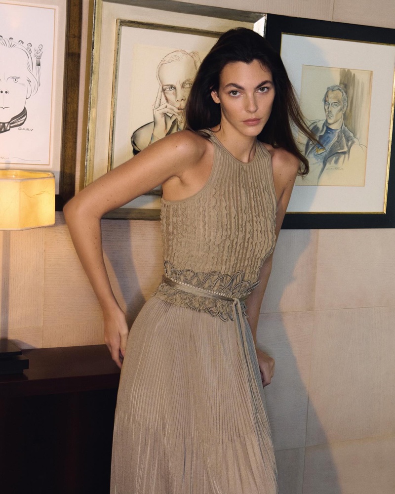 Model Vittoria Ceretti in a beige dress standing indoors against framed portraits for Giorgio Armani Spring 2026 campaign
