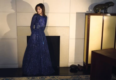 Vittoria Ceretti in a sparkly blue long-sleeved evening gown standing in front of a fireplace for Giorgio Armani.