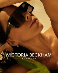 Victoria Beckham wearing oversized black sunglasses and hoop earrings in a close-up portrait for an eyewear campaign.