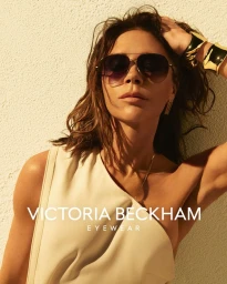 Victoria Beckham wearing oversized sunglasses and a cream sleeveless top against a textured wall