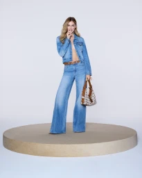 Chiara Ferragni wearing a denim jacket and flared jeans holding a patterned handbag on a circular stage for Guess