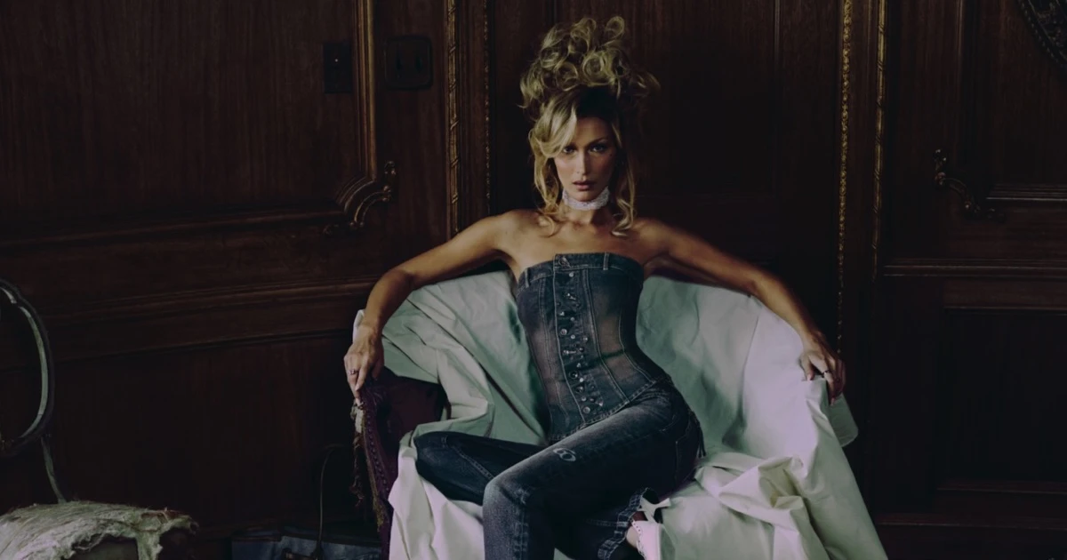 Bella Hadid in a denim outfit seated on a draped armchair against dark wood paneling for Miss Sixty