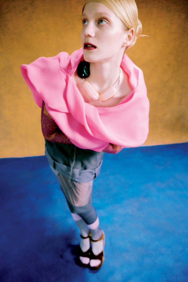 Fashionable woman poses in high-fashion couture with pink wrap and blue floor. Her gaze is upward with high-key studio lighting.