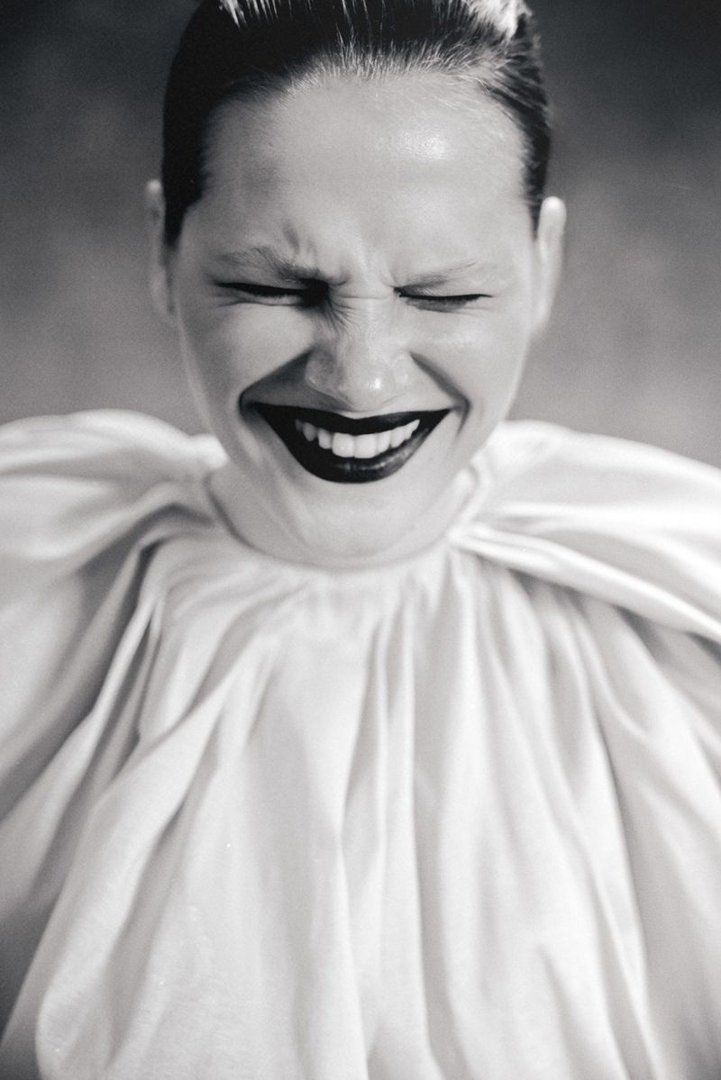 Monochrome portrait of a woman with slicked-back hair, closed eyes, dark lipstick, and wearing a large white ruffled collar.