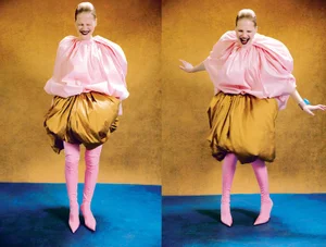 Model in voluminous pink top and golden skirt wearing pink boots against a textured backdrop