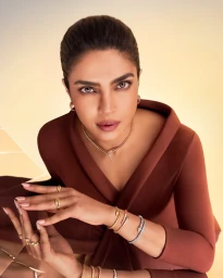Priyanka Chopra wearing Bulgari Serpenti jewelry and a brown V-neck dress against a warm gradient background