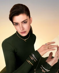 Anne Hathaway wearing a dark green turtleneck and Bulgari Serpenti jewelry against a sunset sky background