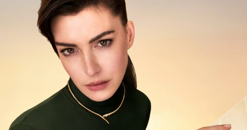 Anne Hathaway wearing a gold snake necklace and a dark green turtleneck against a warm gradient background for Bulgari Serpenti Icon.
