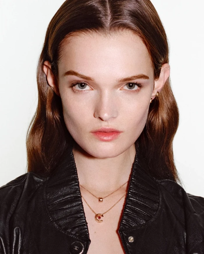Close-up portrait of model Lulu Tenney wearing Chanel Coco Crush gold necklaces and a black leather jacket against a white background.