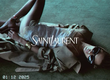 Bella Hadid lying on a carpeted floor wearing sunglasses and a trench coat for Yves Saint Laurent