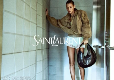 Bella Hadid in a brown jacket and shorts holding a black leather handbag inside a tiled elevator by Yves Saint Laurent
