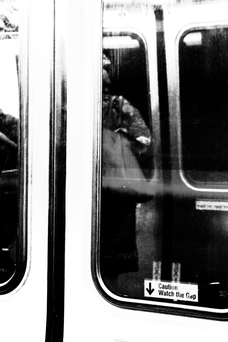 Monochrome image of a subway train door with a blurry view of an adult, an arrow, and caution text, creating a stark contrast.