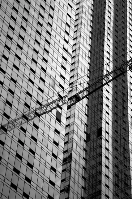 Monochrome photograph of a modern high-rise building with a geometric grid of windows and a partial view of a construction crane.