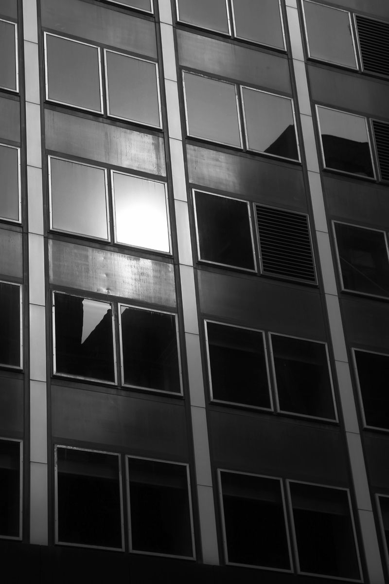 Exterior of a tall building with repeating windows, photographed in black and white. The angle emphasizes the building's height.
