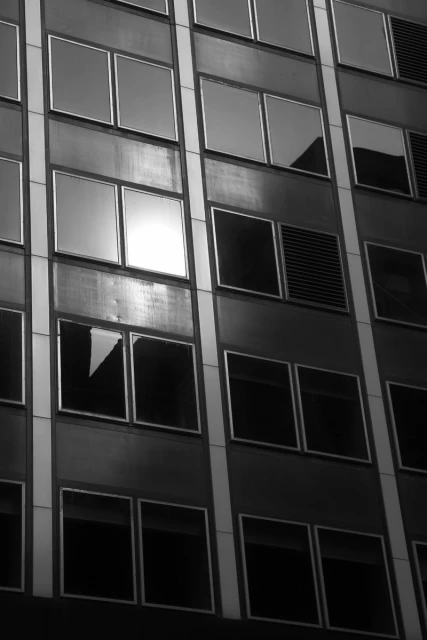 Exterior of a tall building with repeating windows, photographed in black and white. The angle emphasizes the building's height.