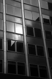Low angle monochrome photograph of a multi-story building facade featuring a repetitive grid of rectangular windows.